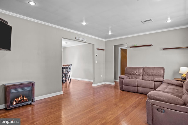 living area featuring visible vents, ornamental molding, a glass covered fireplace, wood finished floors, and baseboards