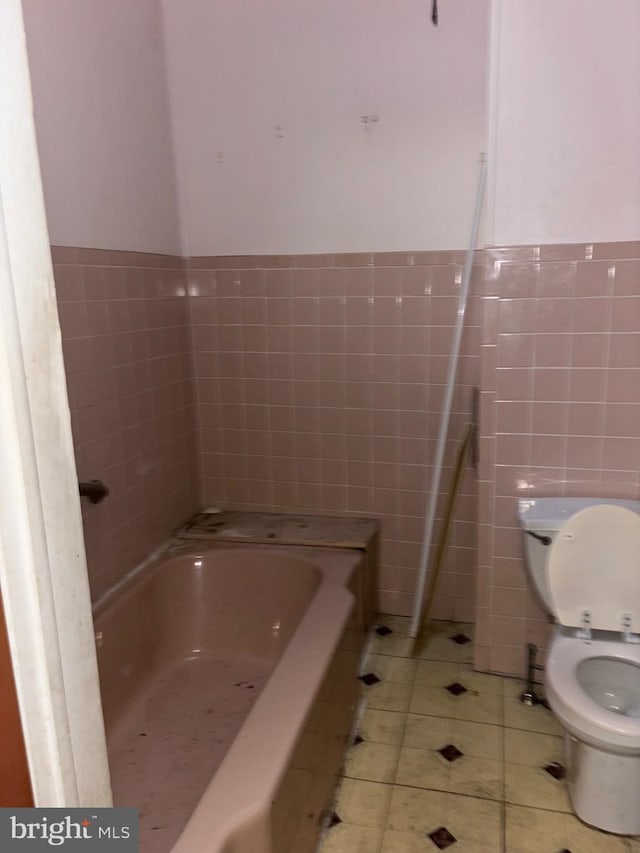 bathroom with tile patterned floors, toilet, tile walls, and a tub to relax in