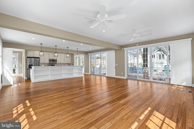 unfurnished living room with light wood-style flooring, a ceiling fan, a sink, recessed lighting, and baseboards