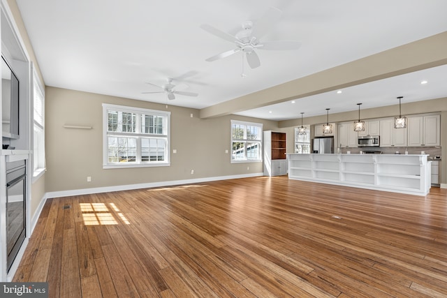 unfurnished living room featuring light wood-type flooring, a ceiling fan, a glass covered fireplace, recessed lighting, and baseboards