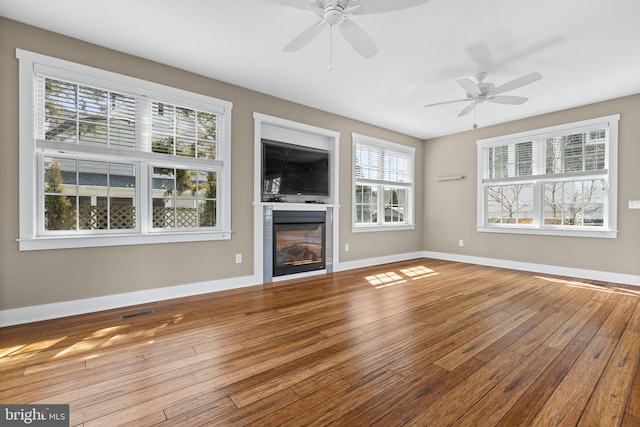 unfurnished living room with a glass covered fireplace, visible vents, baseboards, and hardwood / wood-style flooring