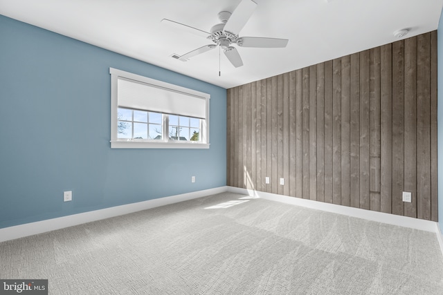 spare room featuring wooden walls, carpet, visible vents, baseboards, and ceiling fan