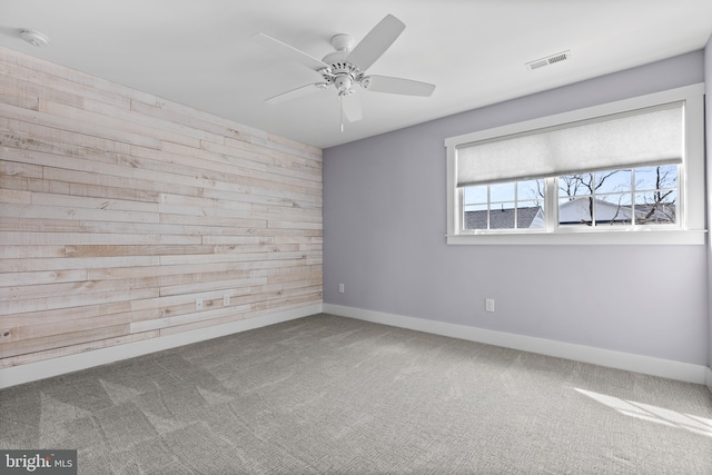 spare room featuring visible vents, carpet floors, wooden walls, baseboards, and ceiling fan