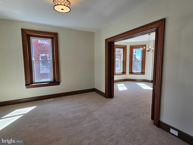 carpeted spare room with a chandelier, visible vents, and baseboards