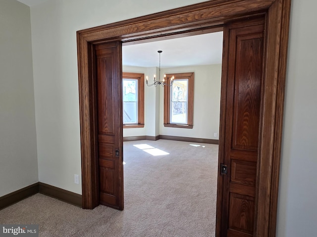 hall featuring a notable chandelier, baseboards, and carpet