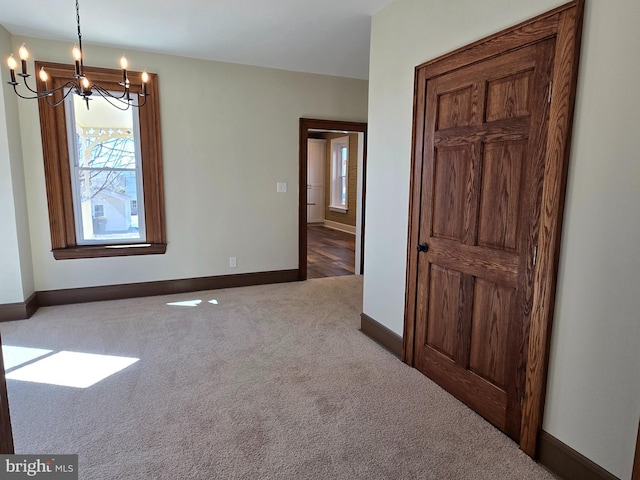 unfurnished room with a notable chandelier, baseboards, and carpet