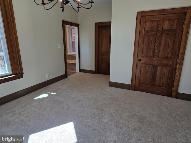 carpeted spare room featuring an inviting chandelier and baseboards