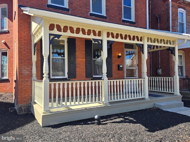 view of exterior entry with a porch and brick siding