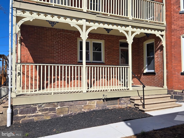 view of exterior entry with brick siding, covered porch, and a balcony