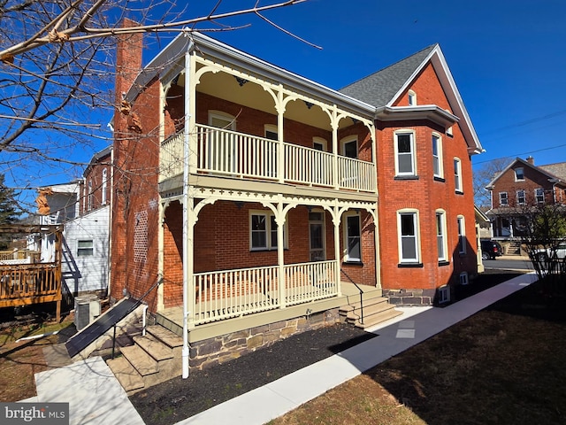 view of front of house featuring a chimney, brick siding, a porch, and a balcony