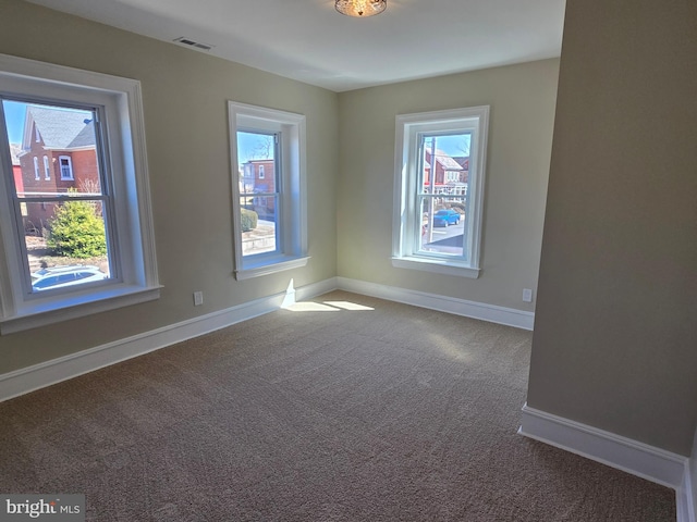 carpeted empty room featuring plenty of natural light, baseboards, and visible vents