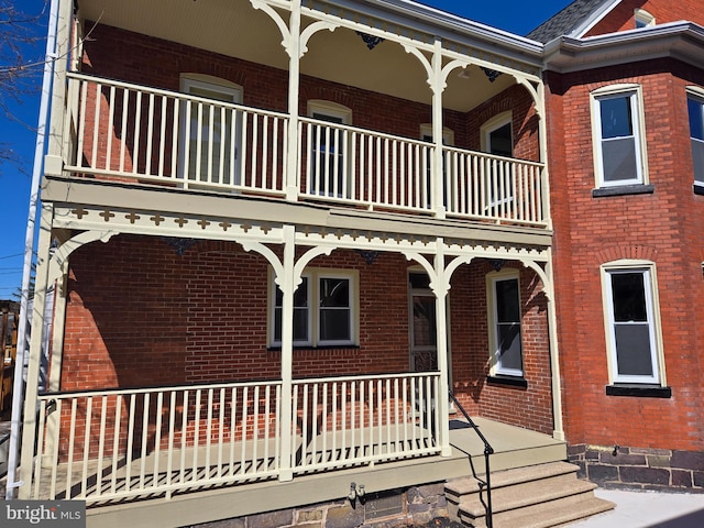 exterior space featuring brick siding, covered porch, and a balcony