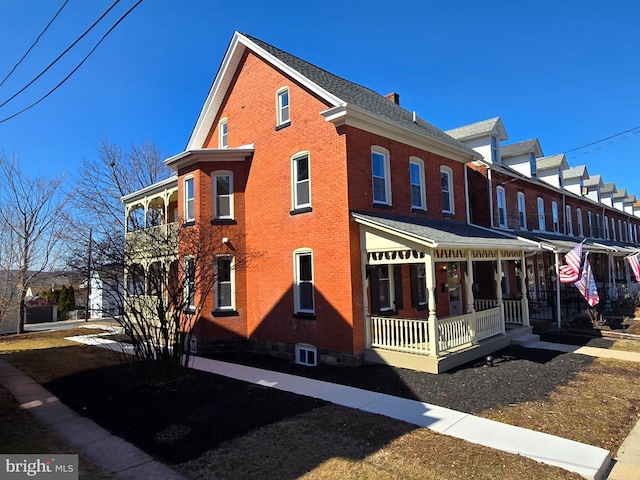 view of side of home with brick siding, a porch, and a chimney