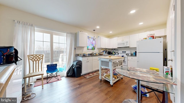 kitchen with white appliances, wood finished floors, recessed lighting, pendant lighting, and white cabinetry