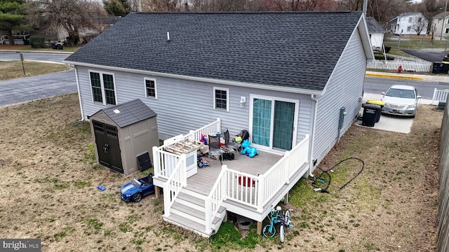 back of property featuring a deck, an outdoor structure, a storage shed, and a shingled roof