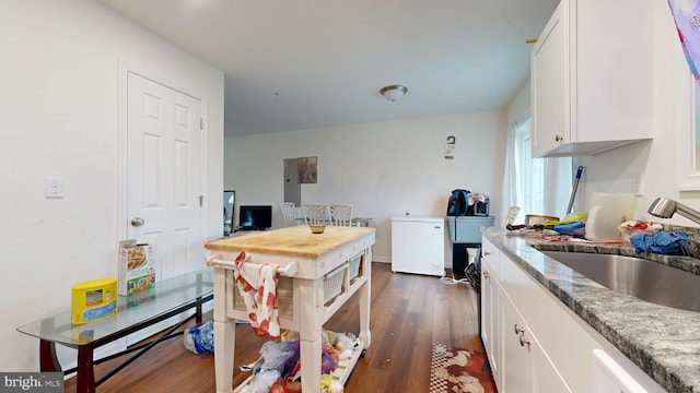 kitchen with light stone counters, dark wood-style floors, a sink, white cabinetry, and fridge