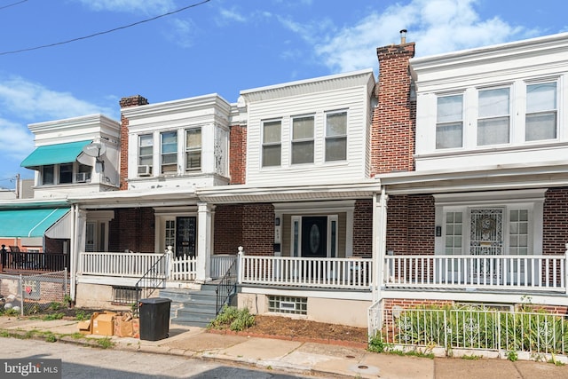 townhome / multi-family property featuring brick siding, covered porch, and a chimney