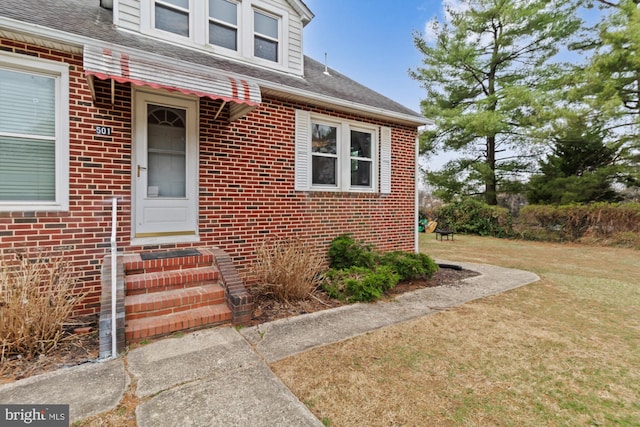 property entrance with brick siding, a lawn, and a shingled roof