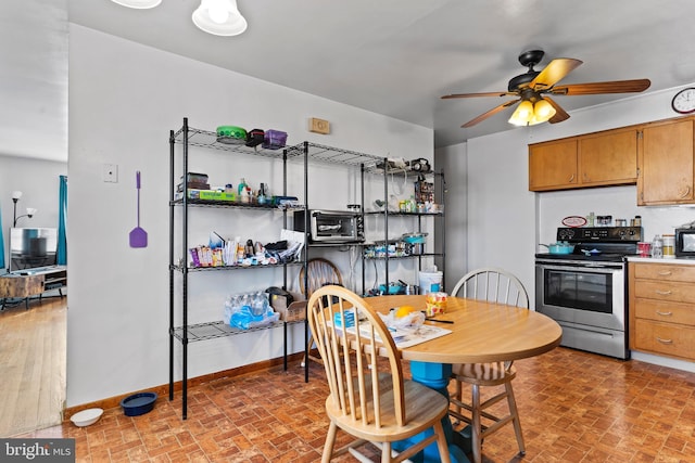 kitchen featuring baseboards, stainless steel electric range oven, brick floor, and a ceiling fan