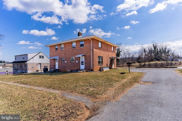 view of home's exterior with driveway, a yard, a chimney, entry steps, and brick siding