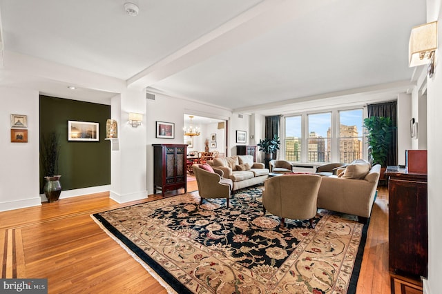 living room featuring beam ceiling, a notable chandelier, wood finished floors, and baseboards