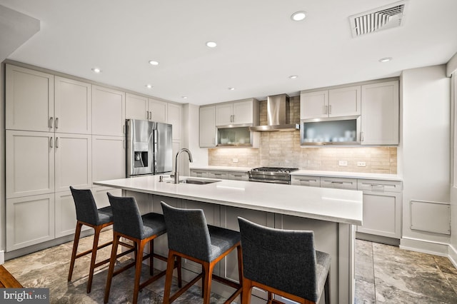 kitchen with visible vents, a sink, appliances with stainless steel finishes, wall chimney range hood, and decorative backsplash