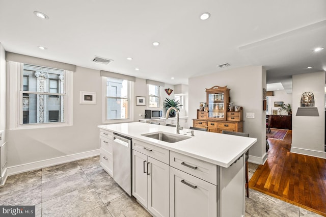 kitchen featuring visible vents, a sink, a center island with sink, light countertops, and stainless steel dishwasher