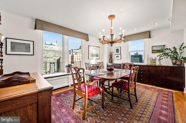 dining area featuring wood finished floors, an inviting chandelier, recessed lighting, a baseboard heating unit, and a view of city