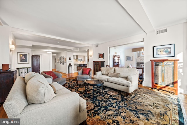 living area featuring visible vents, beamed ceiling, baseboards, and wood finished floors