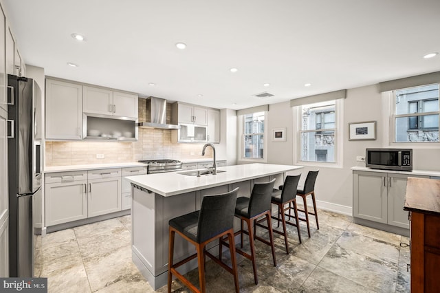 kitchen featuring visible vents, a sink, tasteful backsplash, appliances with stainless steel finishes, and wall chimney exhaust hood