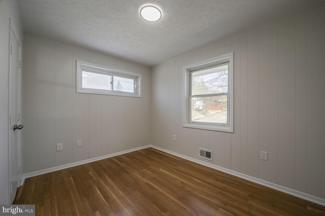 unfurnished room featuring dark wood-type flooring, visible vents, baseboards, and a textured ceiling