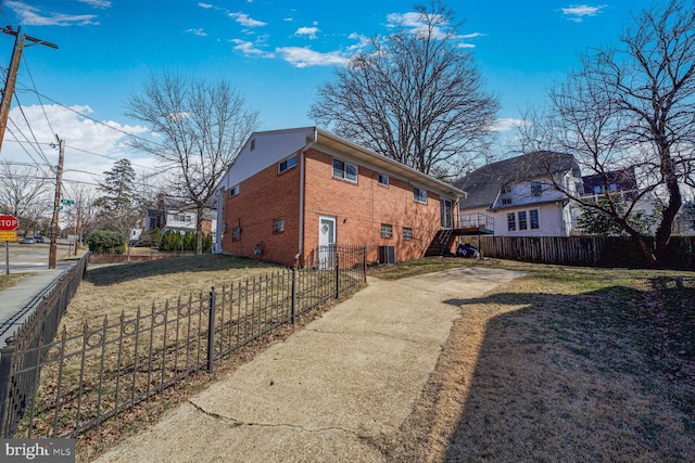 view of side of home featuring brick siding, fence private yard, stairs, central AC unit, and a yard