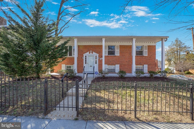 raised ranch featuring brick siding, covered porch, and a fenced front yard