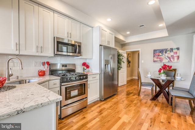 kitchen with visible vents, light wood-style flooring, a sink, backsplash, and appliances with stainless steel finishes