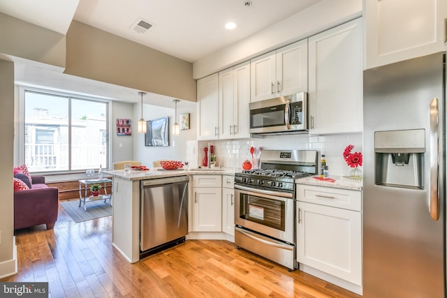 kitchen with visible vents, a peninsula, stainless steel appliances, white cabinetry, and backsplash