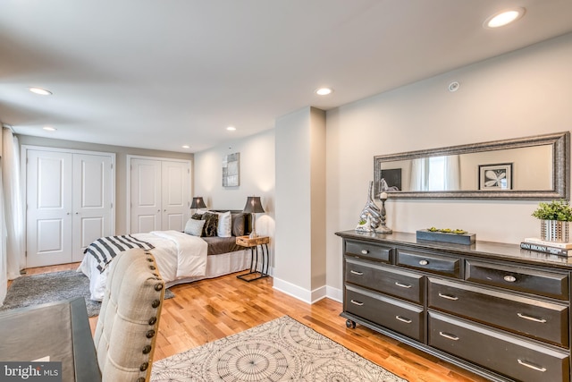 bedroom with light wood finished floors, recessed lighting, baseboards, and two closets