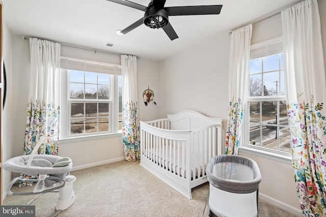 carpeted bedroom with a nursery area, visible vents, baseboards, and ceiling fan