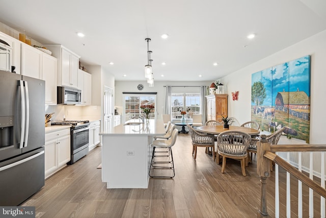 kitchen with white cabinetry, an island with sink, wood finished floors, and appliances with stainless steel finishes