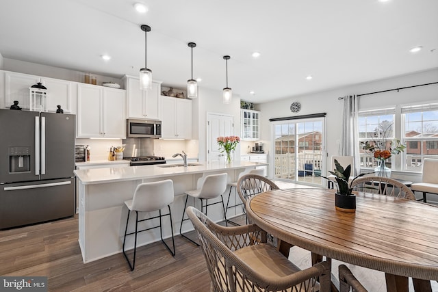 kitchen featuring a center island with sink, dark wood-style flooring, a sink, light countertops, and appliances with stainless steel finishes