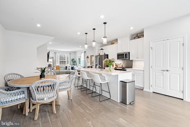 kitchen featuring white cabinetry, a kitchen island with sink, light countertops, appliances with stainless steel finishes, and a kitchen bar