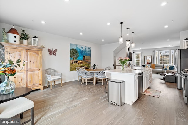 kitchen featuring open floor plan, light countertops, light wood-style flooring, stainless steel appliances, and a sink