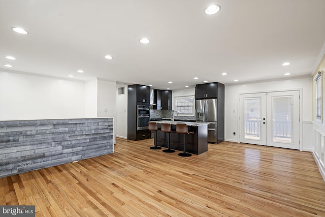 kitchen with light wood-type flooring, ornamental molding, a sink, a kitchen breakfast bar, and appliances with stainless steel finishes