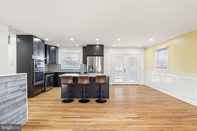 kitchen with decorative backsplash, french doors, light wood-style floors, appliances with stainless steel finishes, and a kitchen bar