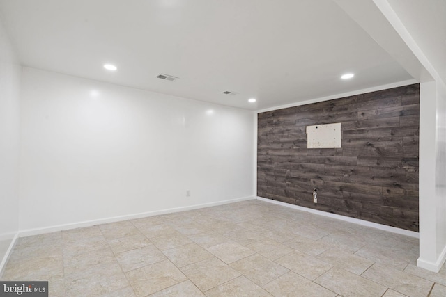 below grade area featuring wooden walls, visible vents, baseboards, recessed lighting, and an accent wall