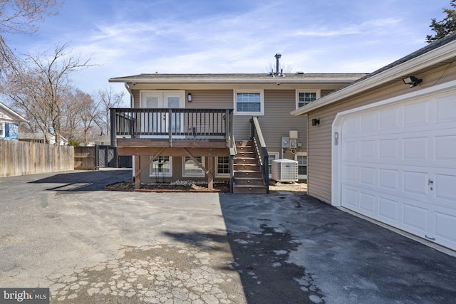 rear view of house featuring driveway, fence, stairway, a garage, and central AC unit