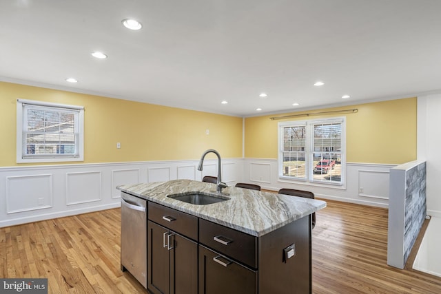 kitchen with dark brown cabinets, dishwasher, light wood-type flooring, light stone counters, and a sink