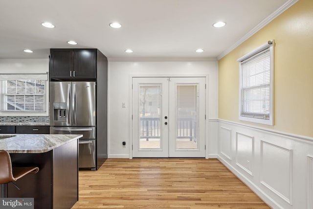 kitchen featuring crown molding, stainless steel fridge with ice dispenser, light stone counters, french doors, and light wood-style floors