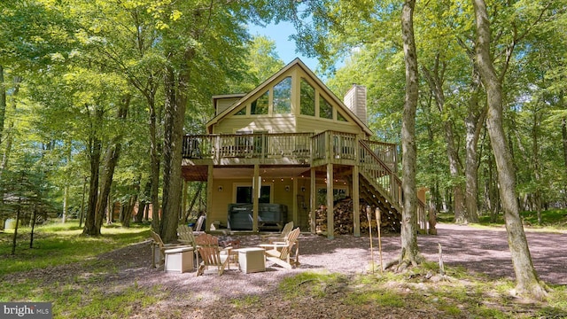 back of property featuring stairway, a chimney, a hot tub, and a wooden deck