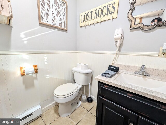 half bathroom with a baseboard radiator, toilet, wainscoting, and tile patterned flooring