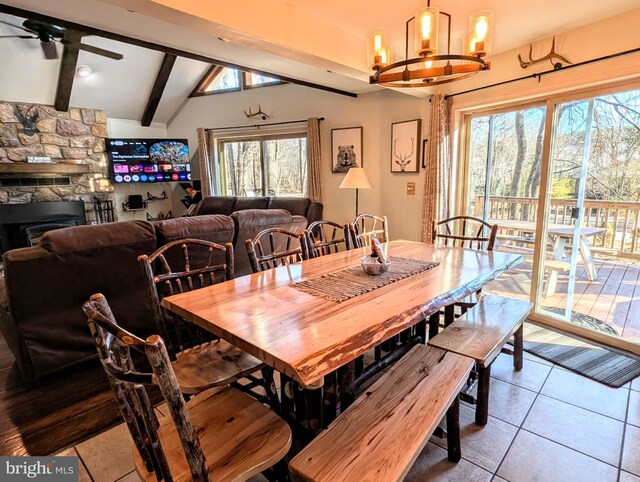 tiled dining space with a fireplace, vaulted ceiling with beams, and ceiling fan with notable chandelier